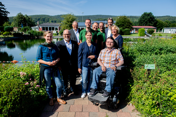 Eine kleine Gruppe Menschen posiert für ein Foto, alle lächeln in die Kamera. Im Hintergrund ist ein Schwimmbecken zu sehen, links uns rechts stehen Büsche.