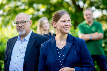 Ministerin Wiebke Osigus ist vorne im Bild zu sehen. Sie lächelt und schaut aus dem Bild hinaus. Neben ihr steht ein Mann, im Hintergrund sind zwei Personen unscharf zu erkennen.