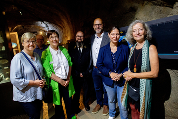 Sechs Personen posieren für ein Gruppenfoto. Im Hintergrund ist ein dunkler Tunnel zu sehen, links im Bild beleuchtete Vitrinen.