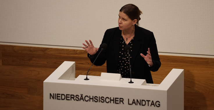 Ministerin Wiebke Osigus steht am Redepult im Plenarsaal des Landtags. Auf dem Rednerpult steht "Niedersächsischer Landtag". Die Ministerin gestikuliert beim Sprechen und hat einen ernsten Gesichtsausdruck.