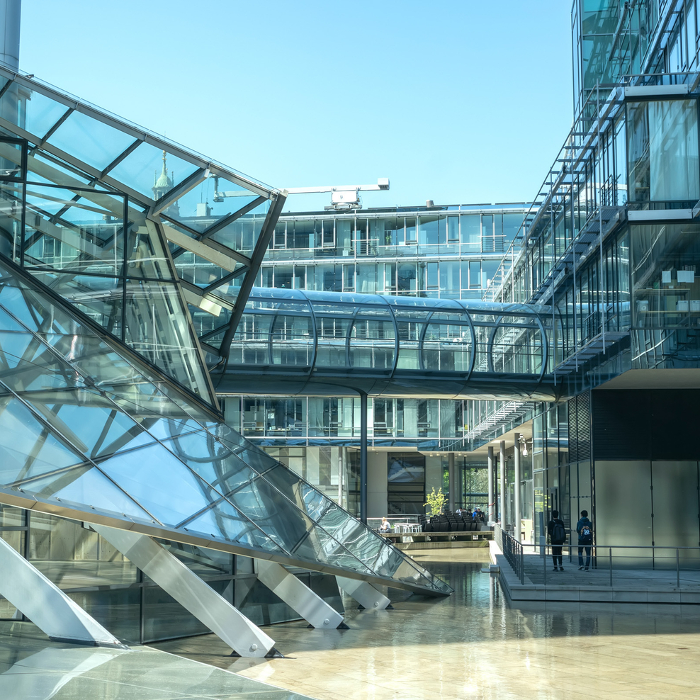 Das Bild zeigt einen Teil eines Glasgebäudekomplexes. Der Himmel im Hintergrund ist wolkenlos.