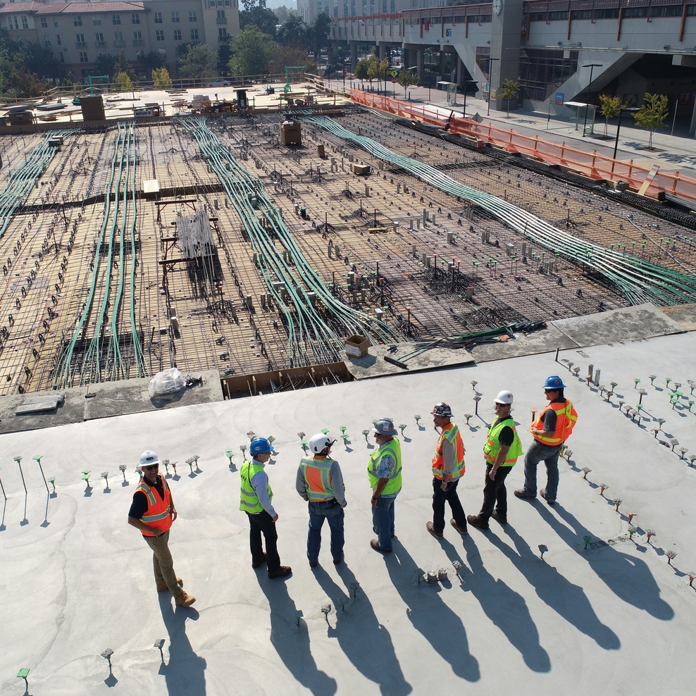 Sieben Personen stehen mit Helmen und Warnwesten stehen auf einer Baustelle.