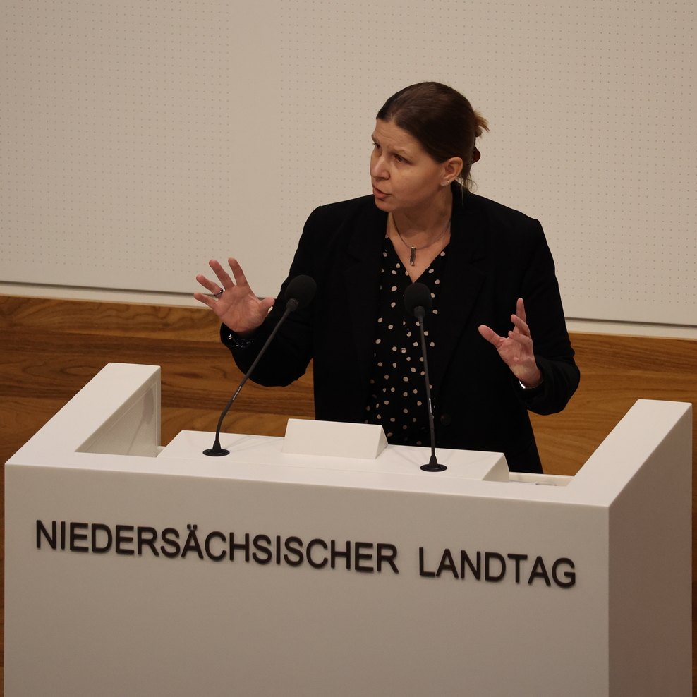 Ministerin Wiebke Osigus steht am Redepult im Plenarsaal des Landtags. Auf dem Rednerpult steht "Niedersächsischer Landtag". Die Ministerin gestikuliert beim Sprechen und hat einen ernsten Gesichtsausdruck.