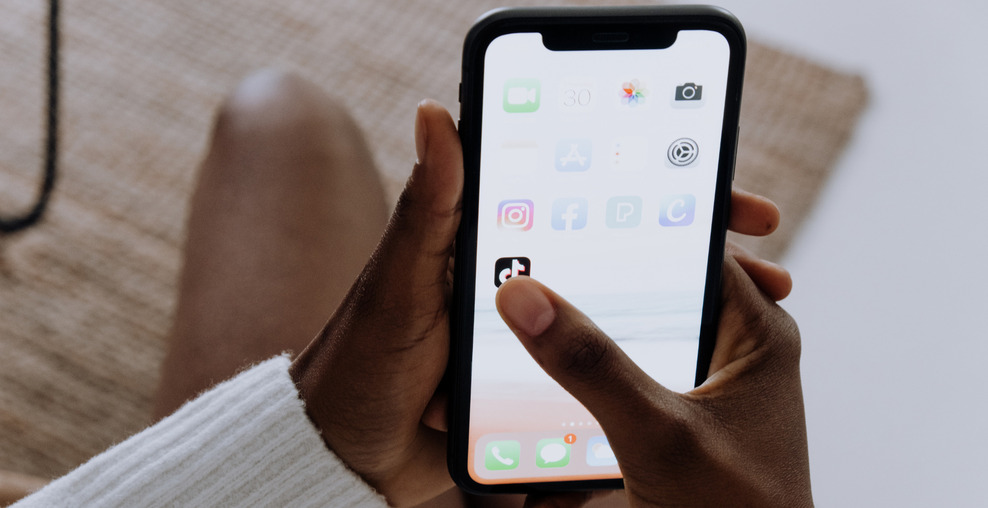 Zwei Hände halten ein Smartphone, der Daumen zeigt auf das Icon der TikTok-App.