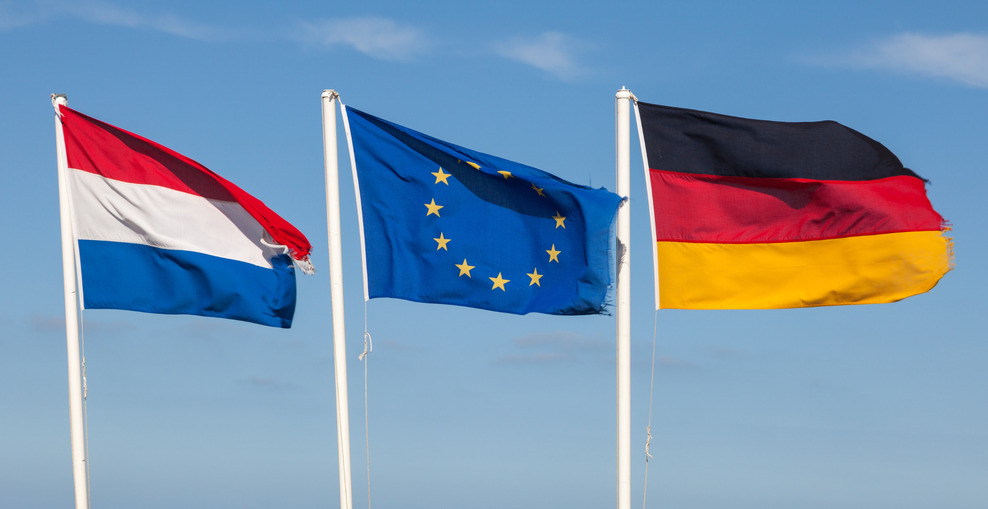 Die Flaggen der Niederlande, der Europäischen Union und von Deutschland wehen vor einem blauen Himmel.