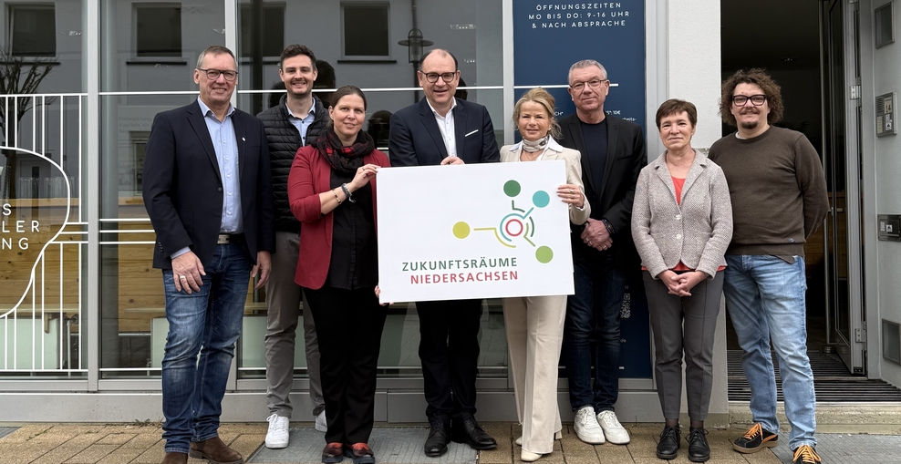 Acht Personen stehen vor der NewKammer in Seesen. Ministerin Wiebke Osigus hält mit zwei weiteren Personen ein Schild mit der Aufschrift Zukunftsräume Niedersachsen. Alle lächeln in die Kamera.