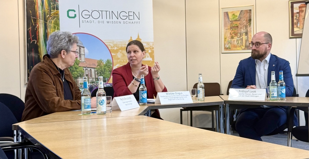 Drei Personen sitzen an einem Tisch, Ministerin Wiebke Osigus in der Mitte. Sie unterhalten sich miteinander. Im Hintergrund steht ein Roll-Up mit der Aufschrift Göttingen - Stadt, die Wissen schafft